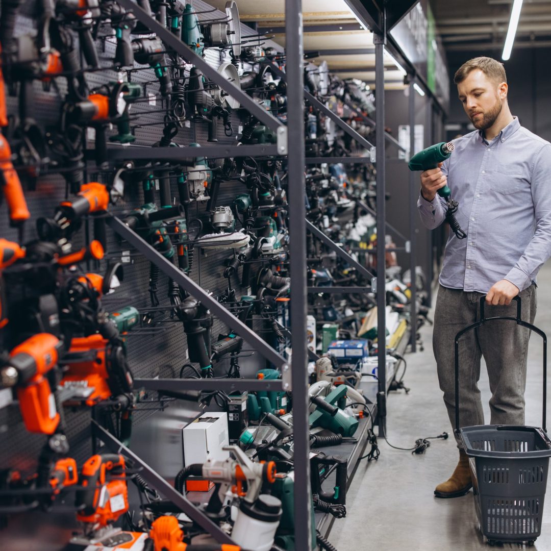 Man examining a power drill in a large hardware store, shopping for tools for home improvements and professional use