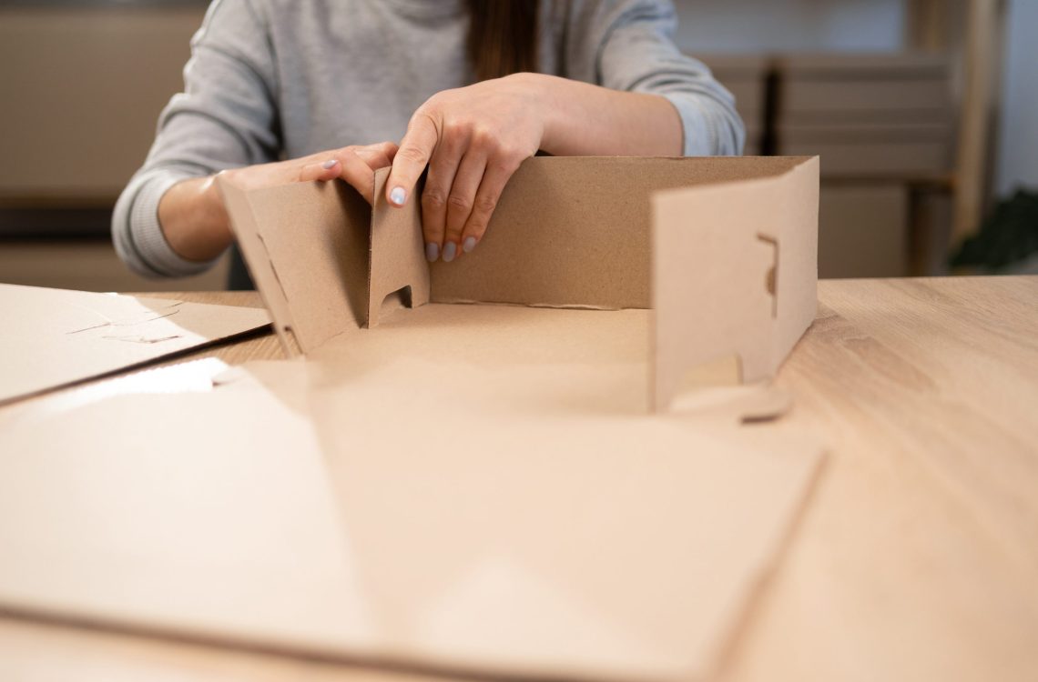 woman small business owner working in home office assembling cardboard box preparing product orders for online shipping. close-up